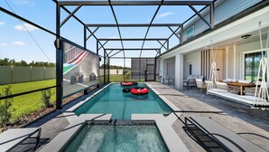 A swimming pool with a covered area, a lounge with seating, and a view of a sports track. - 10BR house at Windsor Cay Resort (Clermont)