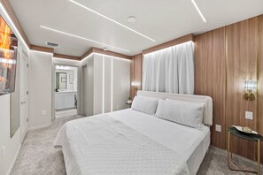 A modern bedroom with a large bed, a wooden headboard, a nightstand, and a wall-mounted lamp. - 10BR house at Windsor Cay Resort (Clermont)