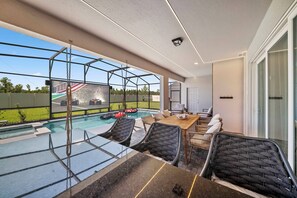 A modern outdoor pool area with a glass enclosure, seating, and a view of a racing track. - 10BR house at Windsor Cay Resort (Clermont)