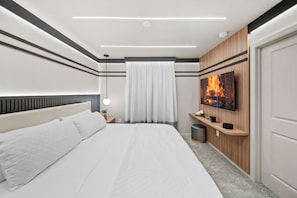 A modern bedroom with a large bed, a bedside table with a lamp, a wall-mounted TV, and a window with curtains. - 10BR house sleeps 27 with private pool (Clermont)