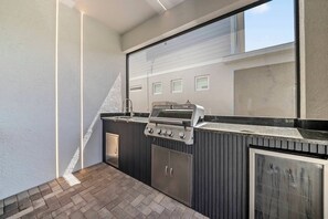 An outdoor kitchen with a grill, built-in cabinets, and a view of a residential building. - 10BR house sleeps 27 with private pool (Clermont)