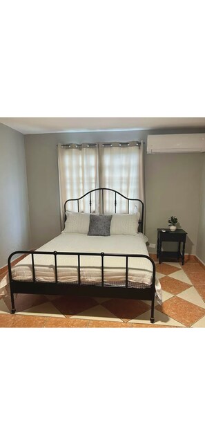 A bed with a metal frame, white bedding, and a small bedside table with a plant. - Modern Loft by LM (Arroyo)