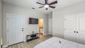 A bedroom with a bed, a ceiling fan, a TV, and a small table with a candle.