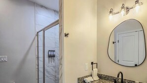 A bathroom with a shower, a sink with a vanity, and a mirror.