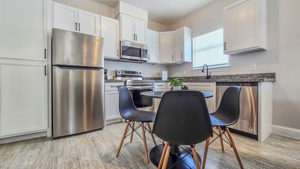 A modern kitchen with stainless steel appliances, white cabinetry, and a dining area with black chairs.