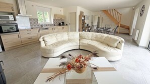 Eine moderne Küche mit eingebauten Geräten, ein Essbereich mit einer Holztreppe und ein Wohnzimmer mit einem weißen Sofa und einer dekorativen Vase.