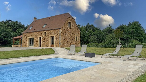 Ein Steinhaus mit Swimmingpool und Liegestühlen.
