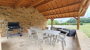 Eine Terrasse im Freien mit einer Steinwand, einem Grill, einem Tisch mit Stühlen und einer Couch.