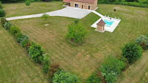 Ein Steinhhaus mit Swimmingpool, umgeben von gepflegtem Rasen und dichter Baumvegetation.