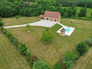 Une maison en pierre avec une piscine, entourée d’une pelouse bien entretenue et d’arbres touffus.
