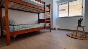 A bunk bed in a room with a window, a small table with a plant, and a doily on the floor. - Apartment in Portimão City Centre (Portimão)