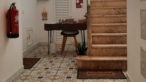 A hallway with patterned floor tiles, a fire extinguisher, a welcome sign, a staircase, and a door with emergency instructions. - Apartment in Portimão City Centre (Portimão)