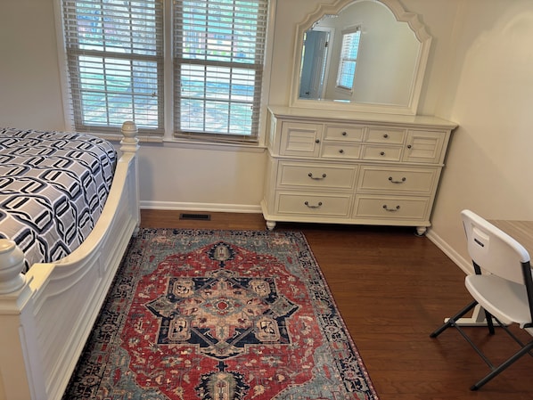 Un dormitorio con cama, cómoda, silla y alfombra.