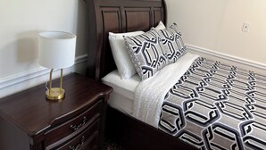 Una cama bien hecha con ropa de cama estampada, una lámpara de noche y una mesita de noche de madera con cajones.