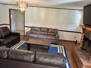 Una sala de estar con un sofá de cuero marrón, un sillón a juego, una mesa de centro de madera y una chimenea de ladrillo.