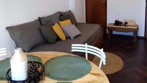 A living room with a sofa, a dining table with placemats, a hanging light fixture, and a door in the background. - Like at Home, Apartment in the center of Cordoba Capital, close to everything! (Córdoba)