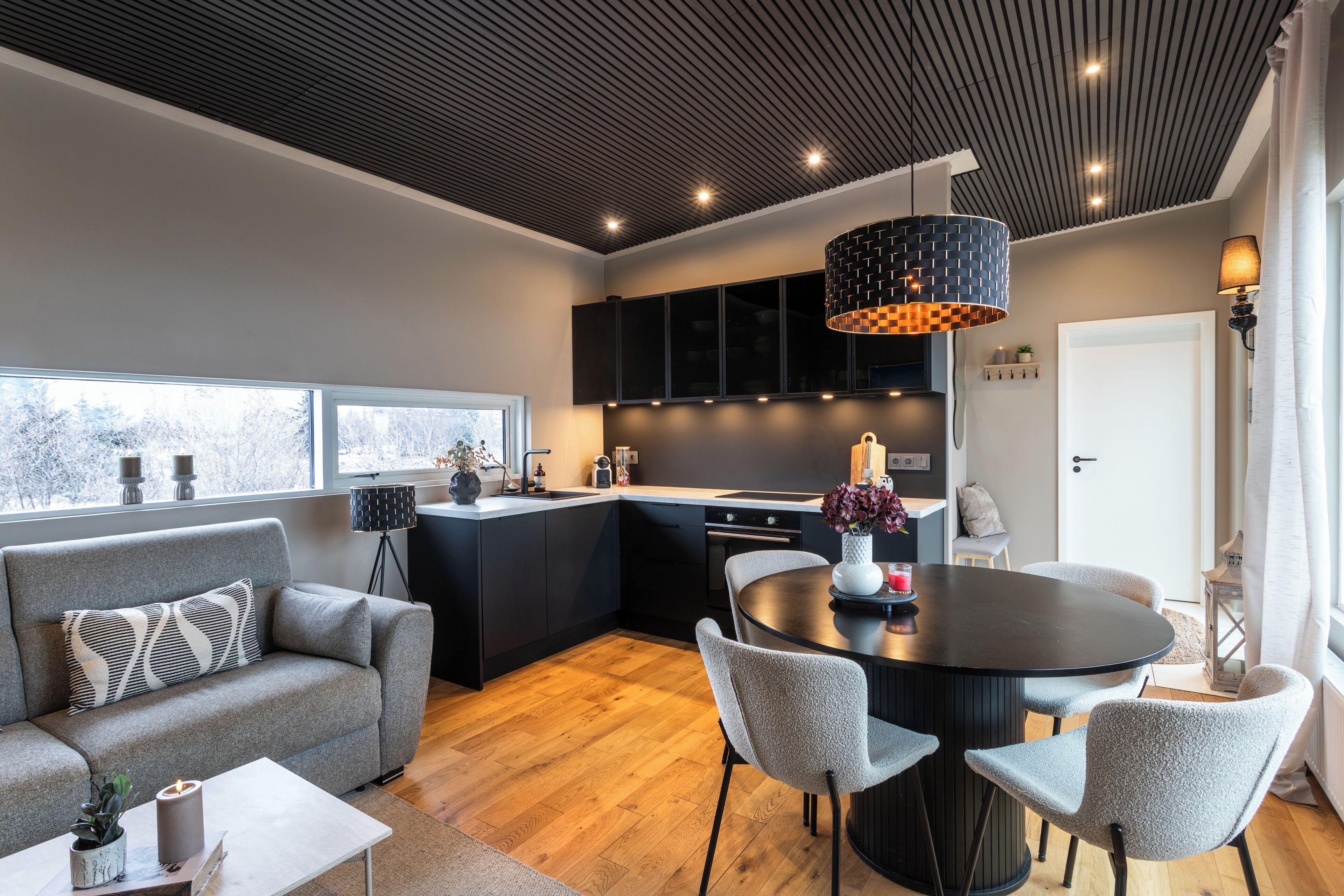 Une cuisine moderne avec des meubles de rangement noirs, une table de salle à manger ronde et un canapé gris.
