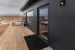 A modern building with a wooden deck, a glass door, and a view of a barren landscape.