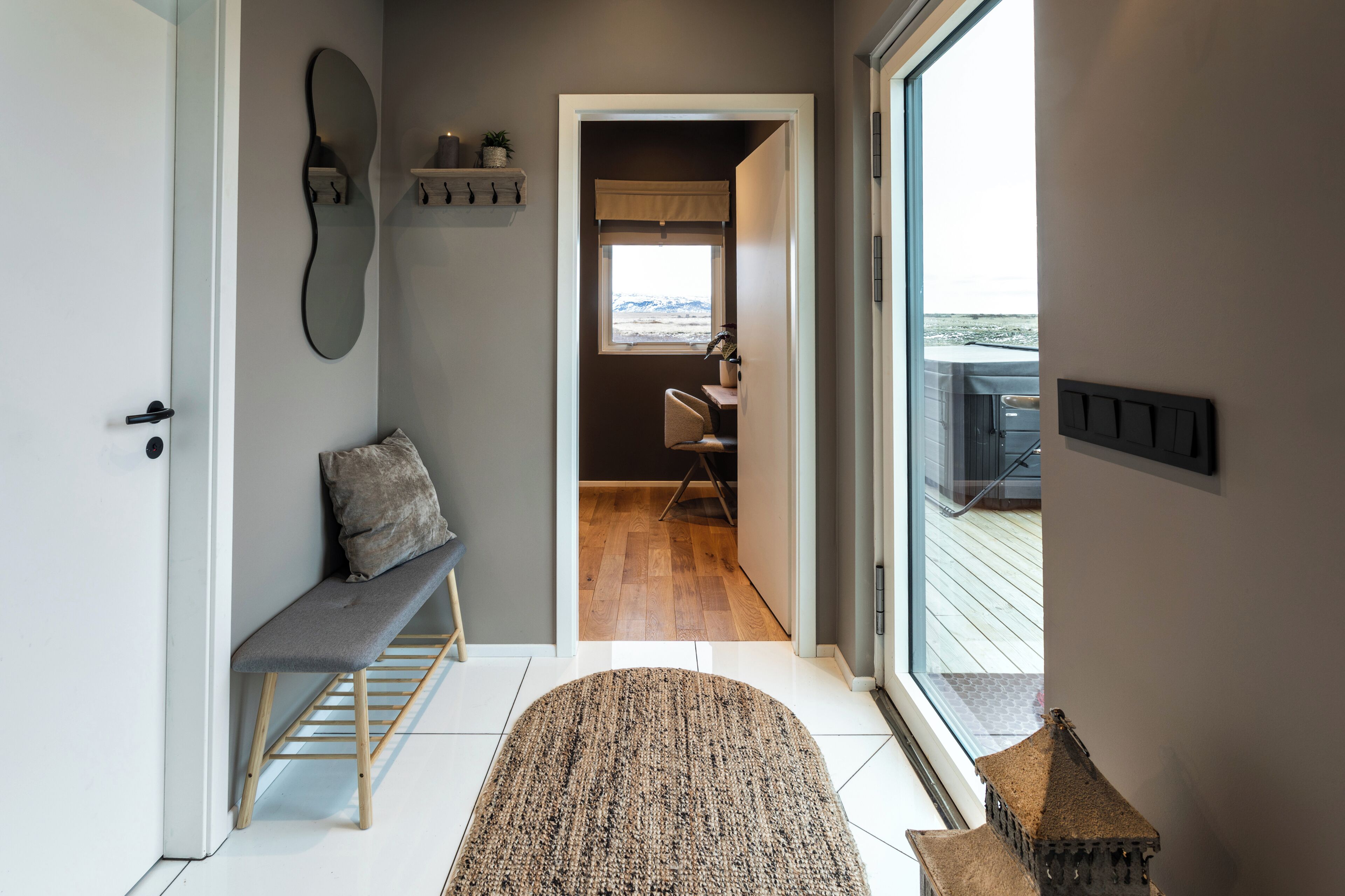 Un couloir avec un banc, un tapis, une petite table et une fenêtre donnant sur une terrasse extérieure.