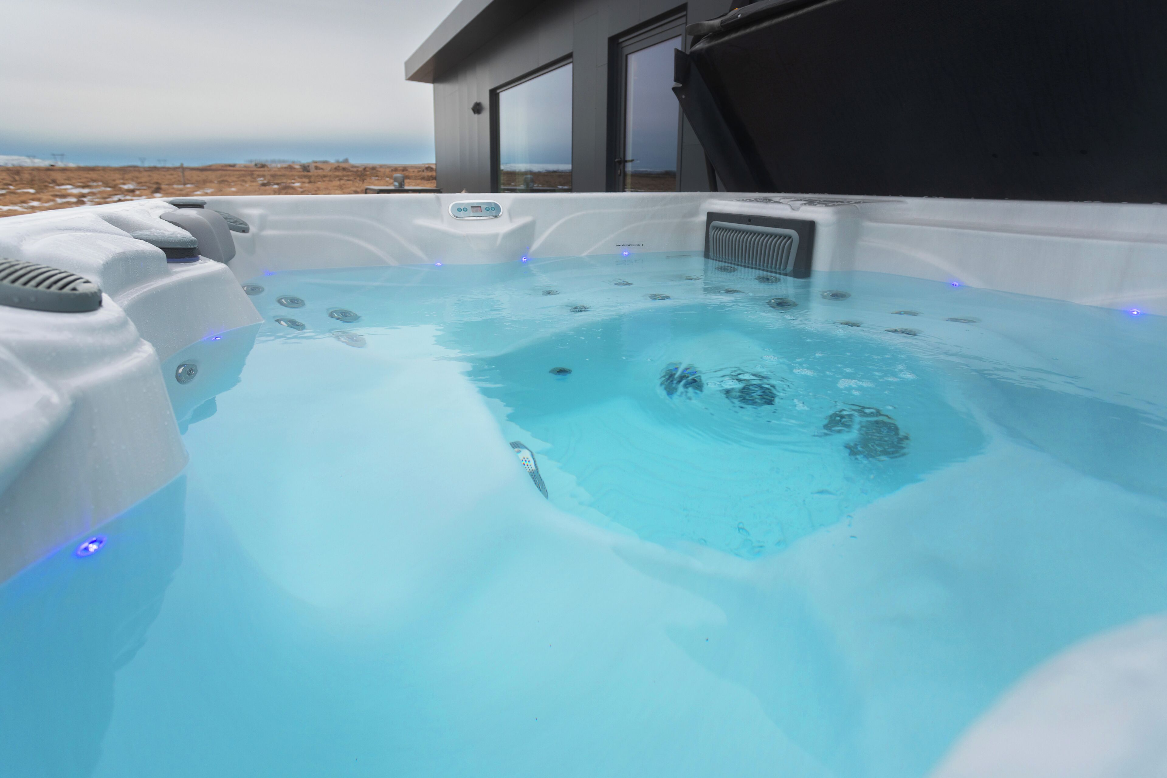 Un bain à remous doté d’un panneau de commande, entouré d’un bâtiment moderne aux grandes fenêtres.