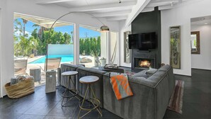 Ein modernes Wohnzimmer mit Kamin, Blick auf einen Pool und einer gemütlichen Sitzecke.