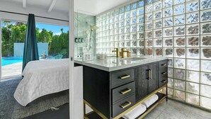 Ein modernes Badezimmer mit einer Duschkabine aus Glas, einem Waschtisch mit goldenen Griffen und Blick auf einen Pool.
