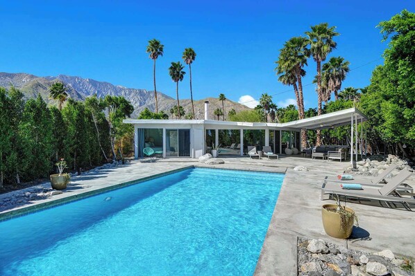 A poolside area with a clear blue pool, lounge chairs, and a modern building with large windows. - 3BR oasis: private pool & mountain views (Palm Springs)