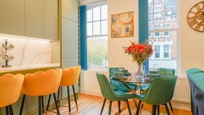 A modern kitchen with a marble countertop, a dining area with green chairs, and a large window with a view of buildings. - Central London Clapham Junction Flat (Clapham Juction, Greater London)