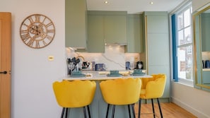 Una cocina con una isla central, armarios verdes y un gran reloj de pared.