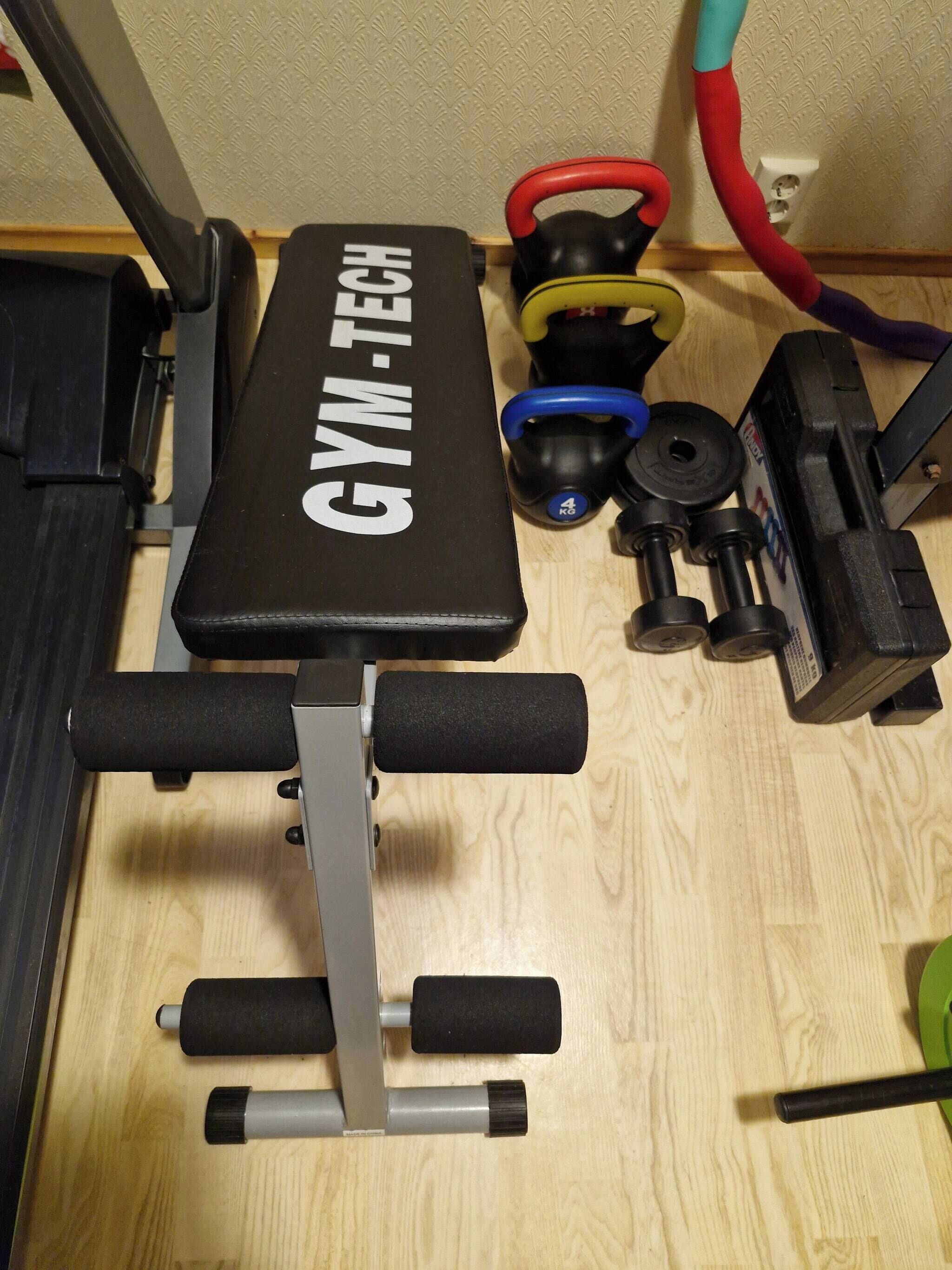 En träningsbänk med viktskivor och kettlebells på ett trägolv.