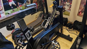 A stationary bike with a digital display, a wall-mounted TV, and sports memorabilia.