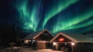 A cabin with a garage and a neon sign, set against a night sky with aurora borealis.
