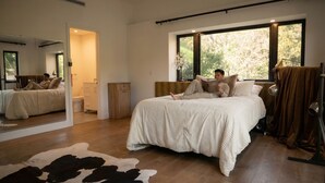 Un dormitorio con una cama grande, un espejo, una ventana con vistas a árboles y una alfombra de cuero de vaca.