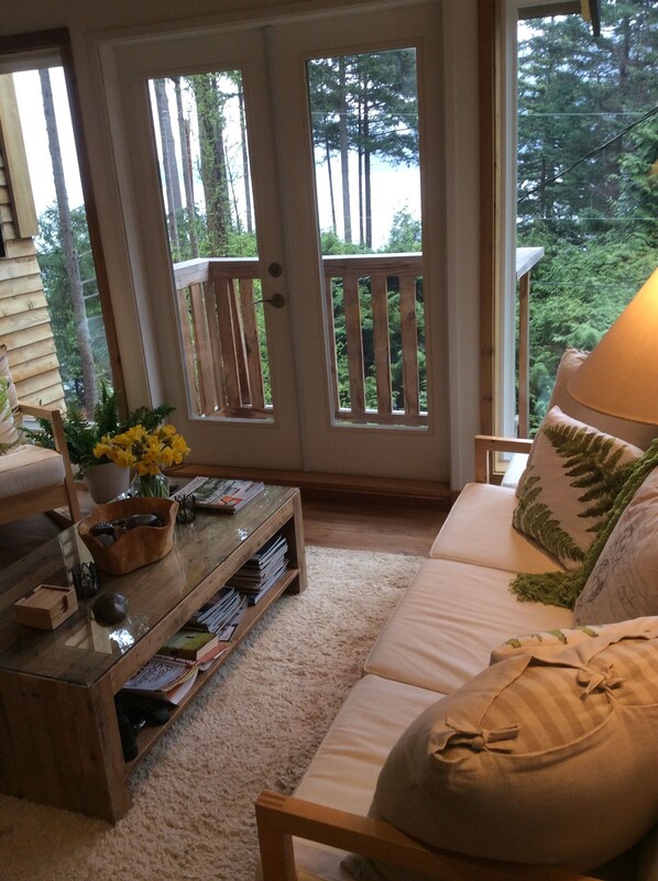 A cozy living room with a wooden coffee table, a sofa, and a view of a forest through a glass door.