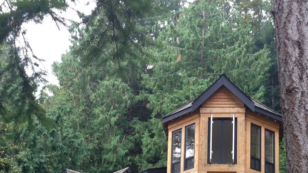 Une cabane en bois dotée d’un balcon, entourée d’une forêt dense.