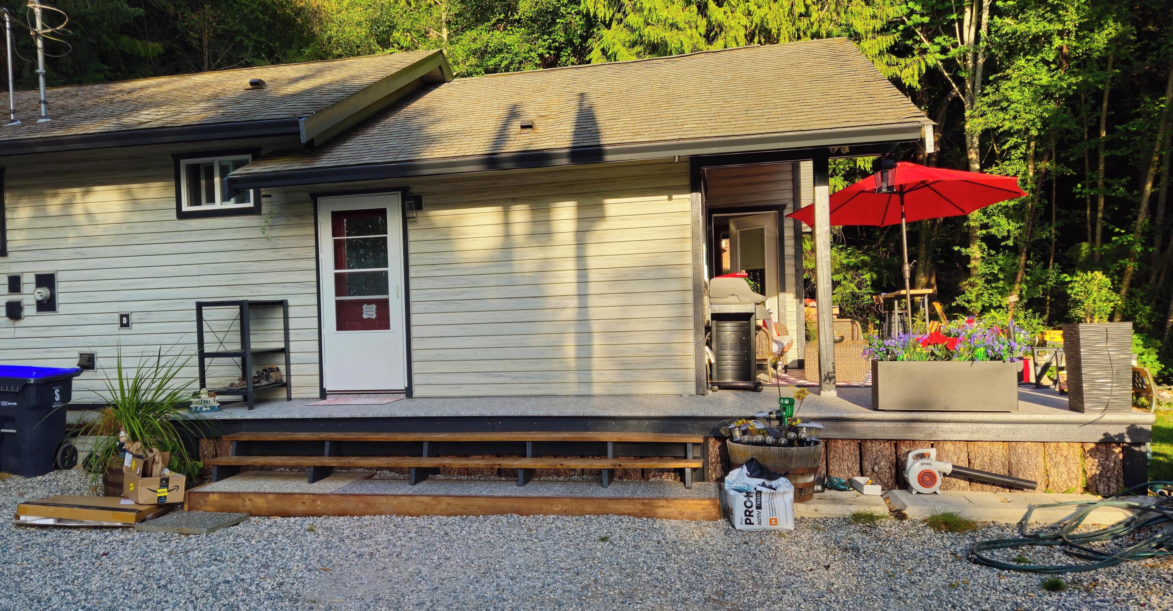 A house with a porch, a red umbrella, and a garden area.