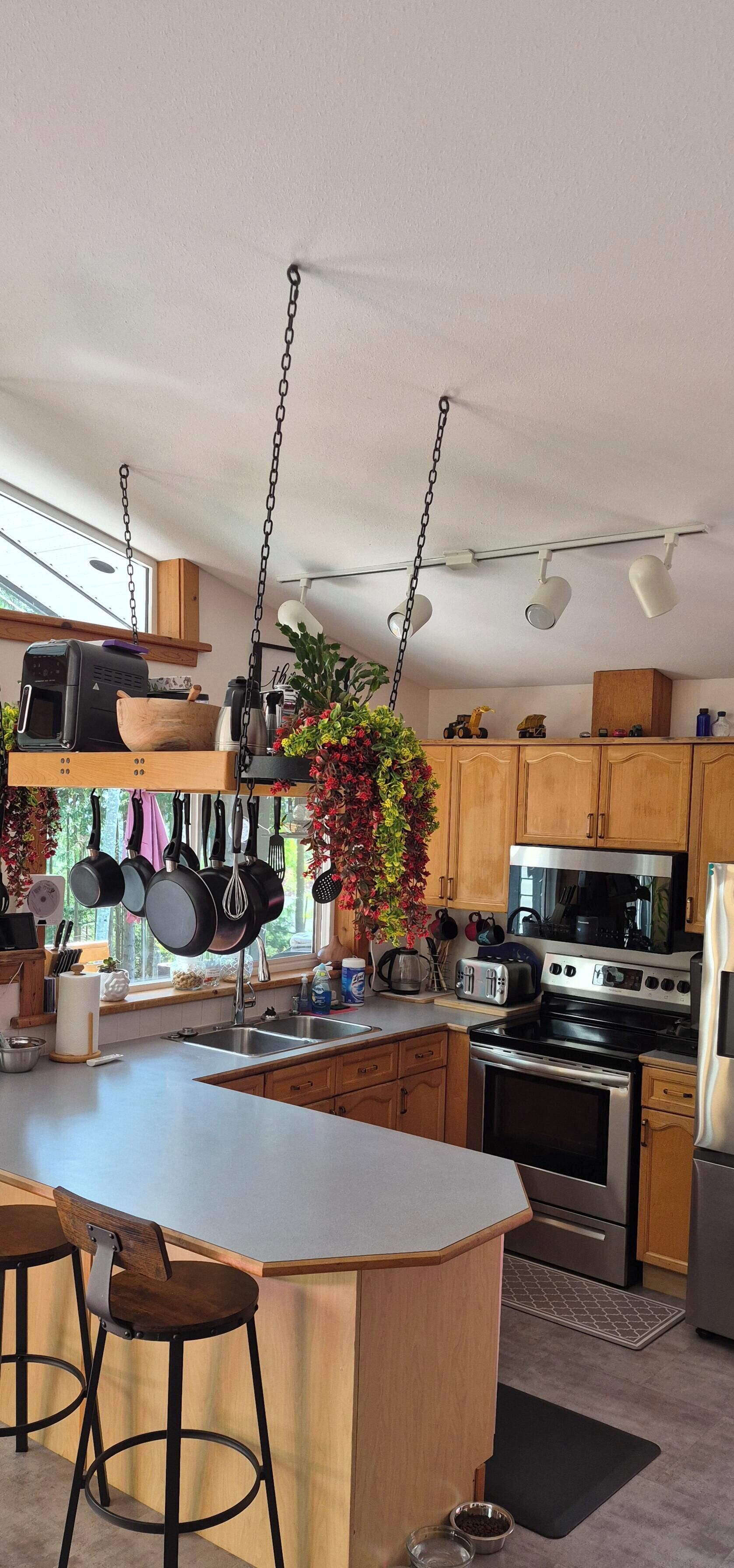A modern kitchen with a central island, hanging pots, and bar stools.