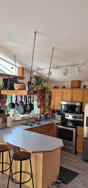 A modern kitchen with a central island, hanging pots, and bar stools.