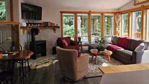 A cozy living room with a fireplace, a television, and large windows offering a view of the outdoors. - SeaView Getaway- B.L.T. (bed and local treats), Retreat. (Sechelt)