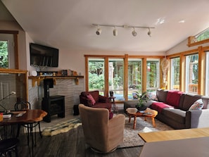 Una sala de estar acogedora con chimenea, televisor y ventanas amplias que ofrecen vistas al exterior.