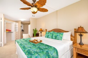 Ein Schlafzimmer mit Bett, Deckenventilator, Nachttisch, Lampe, Schrank und einer Pflanze.