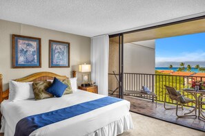 Una camera d'albergo con un letto, un comodino, una lampada, vista sull'oceano e un balcone con sedie e un tavolo.