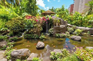 Ein Garten mit einem kleinen Wasserfall, Koi-Karpfen und tropischen Pflanzen.