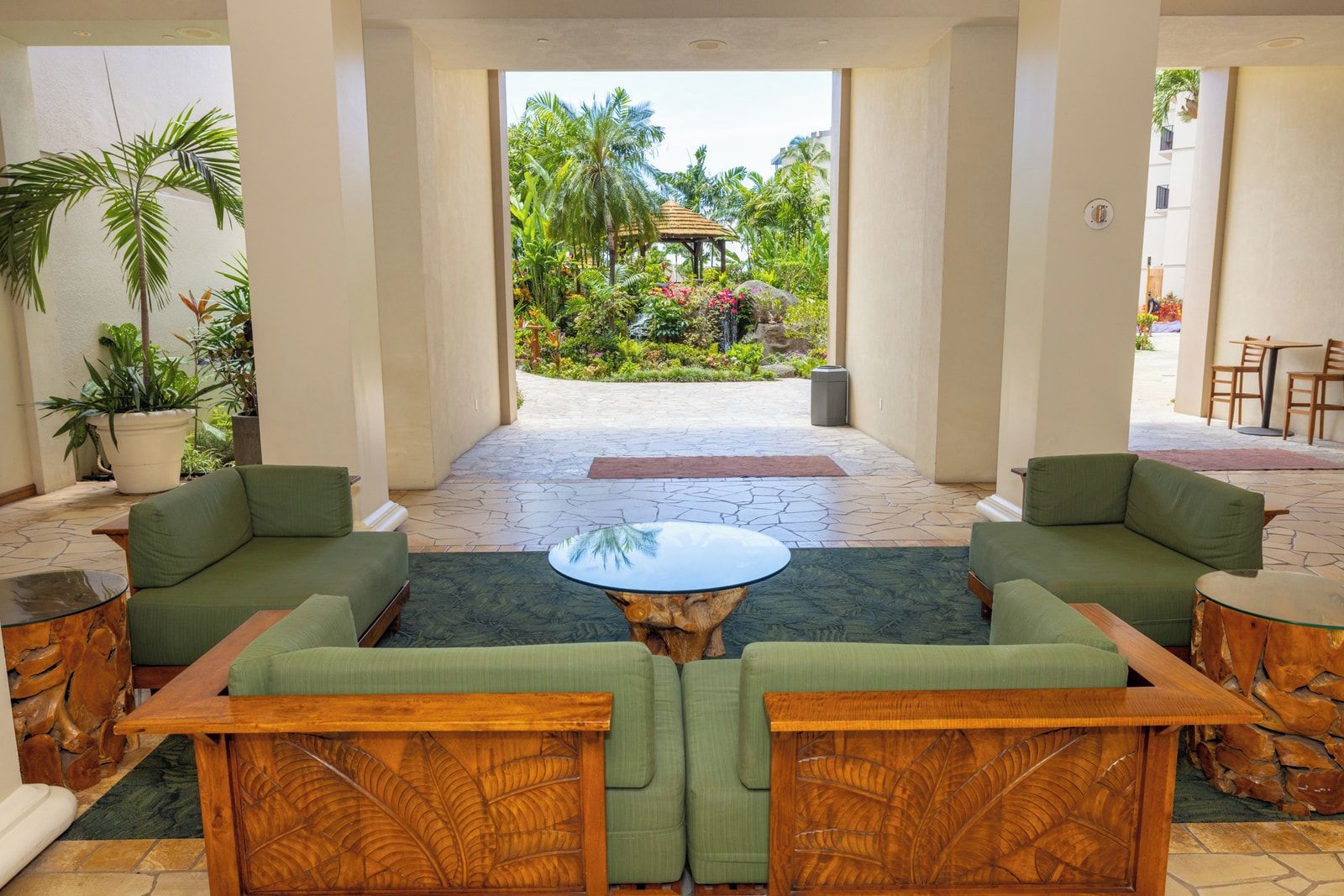 Eine Lobby mit grünen Sofas, einem zentralen Couchtisch und Blick auf einen tropischen Garten.
