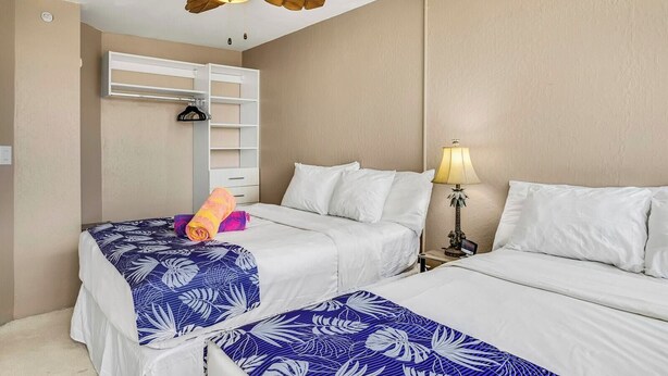 Een hotelkamer met twee bedden, een plafondventilator, een wandairconditioner en een bedlampje.