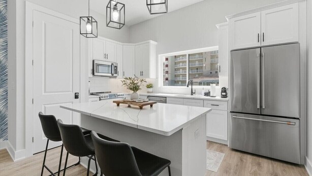 A modern kitchen with white cabinetry, a stainless steel refrigerator, and a central island with bar stools. - Capri-Lux Pool/Hot-Tub/Steps To the Beach (Treasure Island)