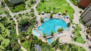 Ein großer Pool, umgeben von Palmen und Liegestühlen, mit einem steinernen Weg, der zum Pool führt.
