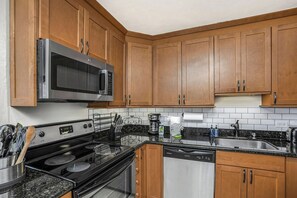 A kitchen with wooden cabinets, a microwave, stove, dishwasher, and granite countertops. - Kaanapali Shores | Ocean View 7 BR, Sleeps 22 | Car Incl. w/ 6+ Nights | KS ML-3773 by KBM (Lahaina)