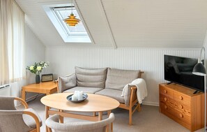 A cozy loft-style room with a sofa, a round table, a TV, and a skylight.