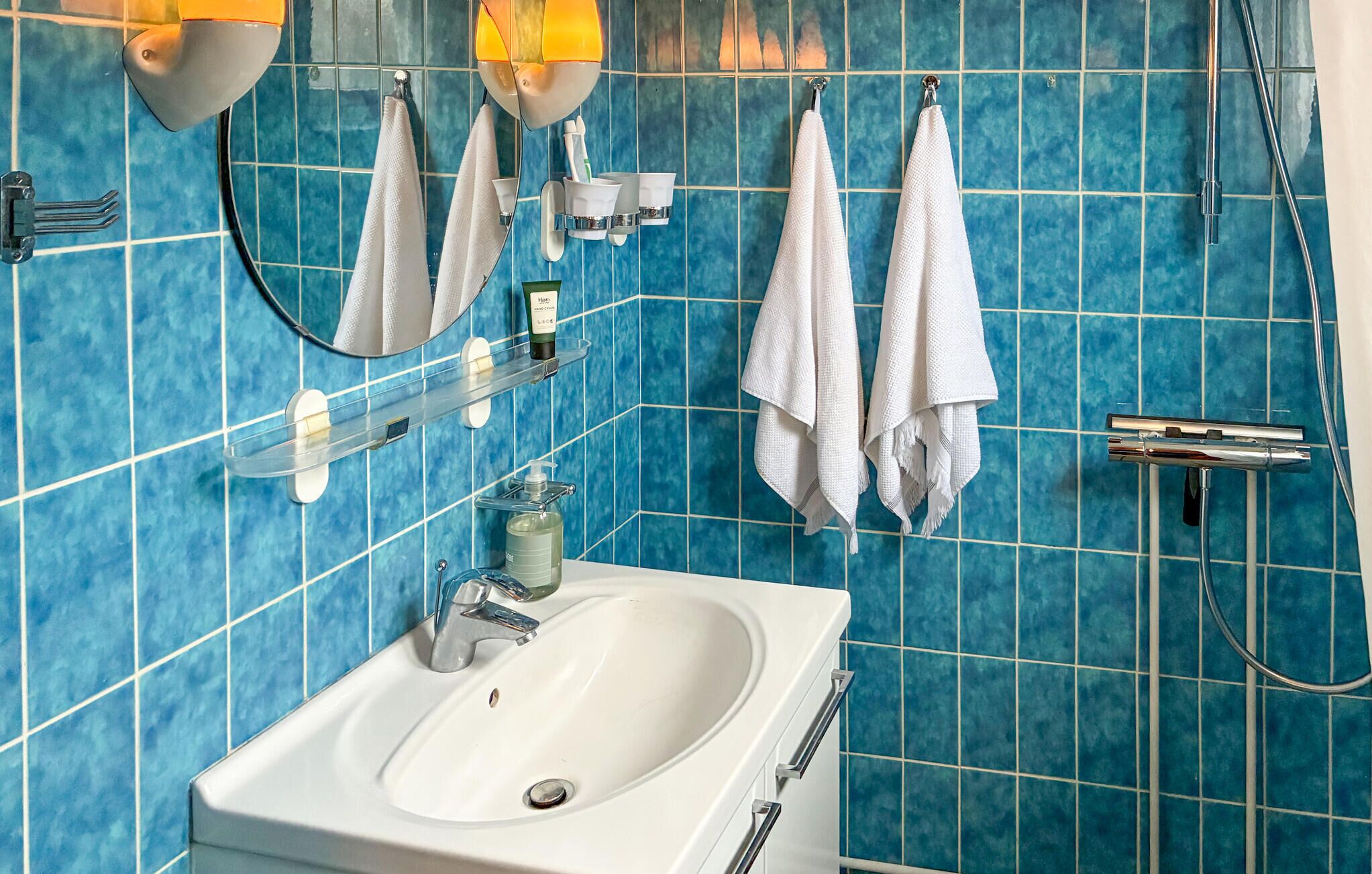 A bathroom with a white sink, blue tiled walls, a mirror, and two white towels hanging on hooks.